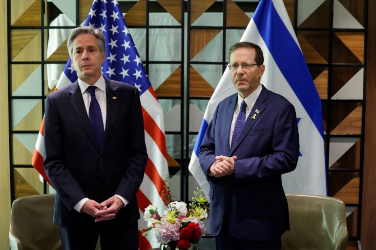 two men stand in front of Israeli and US flags