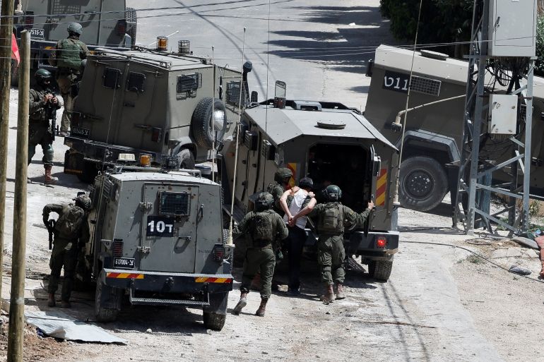Israeli soldiers detain a man near a military vehicle during an Israeli raid in Deir al-Ghusun, in the Israeli occupied West Bank, May 4, 2024. REUTERS/Raneen Sawafta