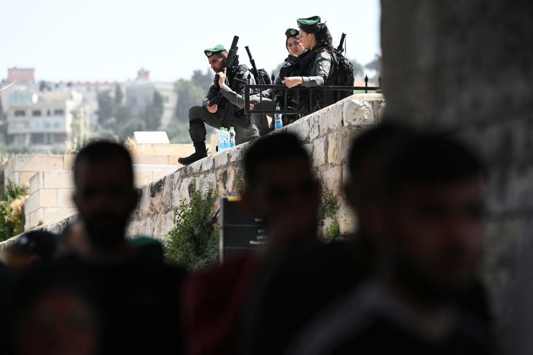 soldiers with large funs look over a wall at people walking beneath