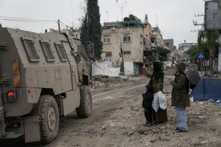 a woman makes a v sign at an army vehicle